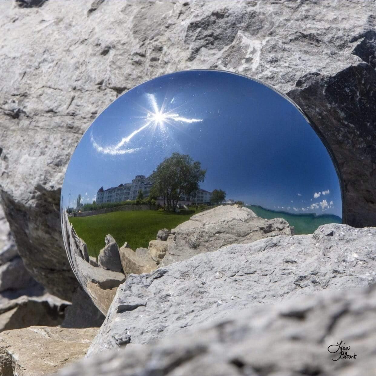 Photo art of gazing ball lodged between two rocks with landscape of bay harbor hotel in reflection by Lisa Blount